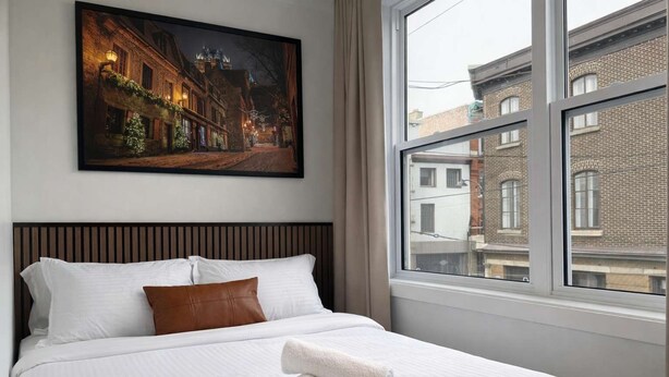 Una camera d'albergo con un letto, un quadro che raffigura una scena di strada e una finestra vista edifici.