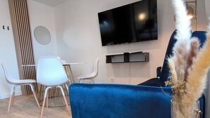 A modern living room with a blue sofa, a round coffee table, and a TV mounted on the wall. - Sublime central T2 (Montélimar)