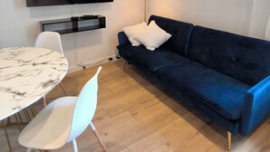 A modern living room with a flat-screen TV, a dark blue sofa, a white chair, a marble table, and a floor lamp. - Sublime central T2 (Montélimar)