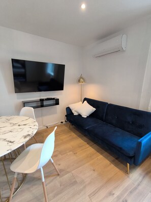 A modern living room with a flat-screen TV, a dark blue sofa, a white chair, a marble table, and a floor lamp. - Sublime central T2 (Montélimar)