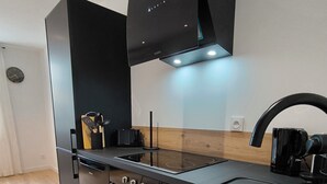 A modern kitchen with a black countertop, stainless steel appliances, and a wooden backsplash. - Sublime central T2 (Montélimar)