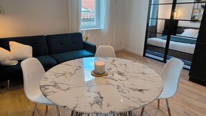 A modern living room with a round marble table, white chairs, a dark blue sofa, and a large window with curtains. - Sublime central T2 (Montélimar)
