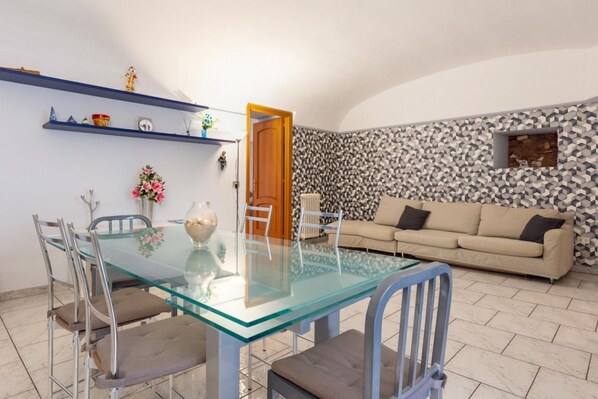 Een eetgedeelte met een glazen tafel en stoelen, een bank en een behangen wand.