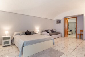 Een slaapkamer met twee bedden, een nachtkastje met een lamp, een bank, een stoel en een deur naar een andere kamer.