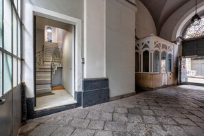 A stone-paved corridor with a staircase leading to a room with a white door and a window. - GuestHost - A welcoming and spacious 136 square meters apartment, perfect for nine people, located on the first floor of the historic Palazzo Pardo (semi-independent entrance, no elevator).The property enjoys an excellent, central location (limited traff (Catania)