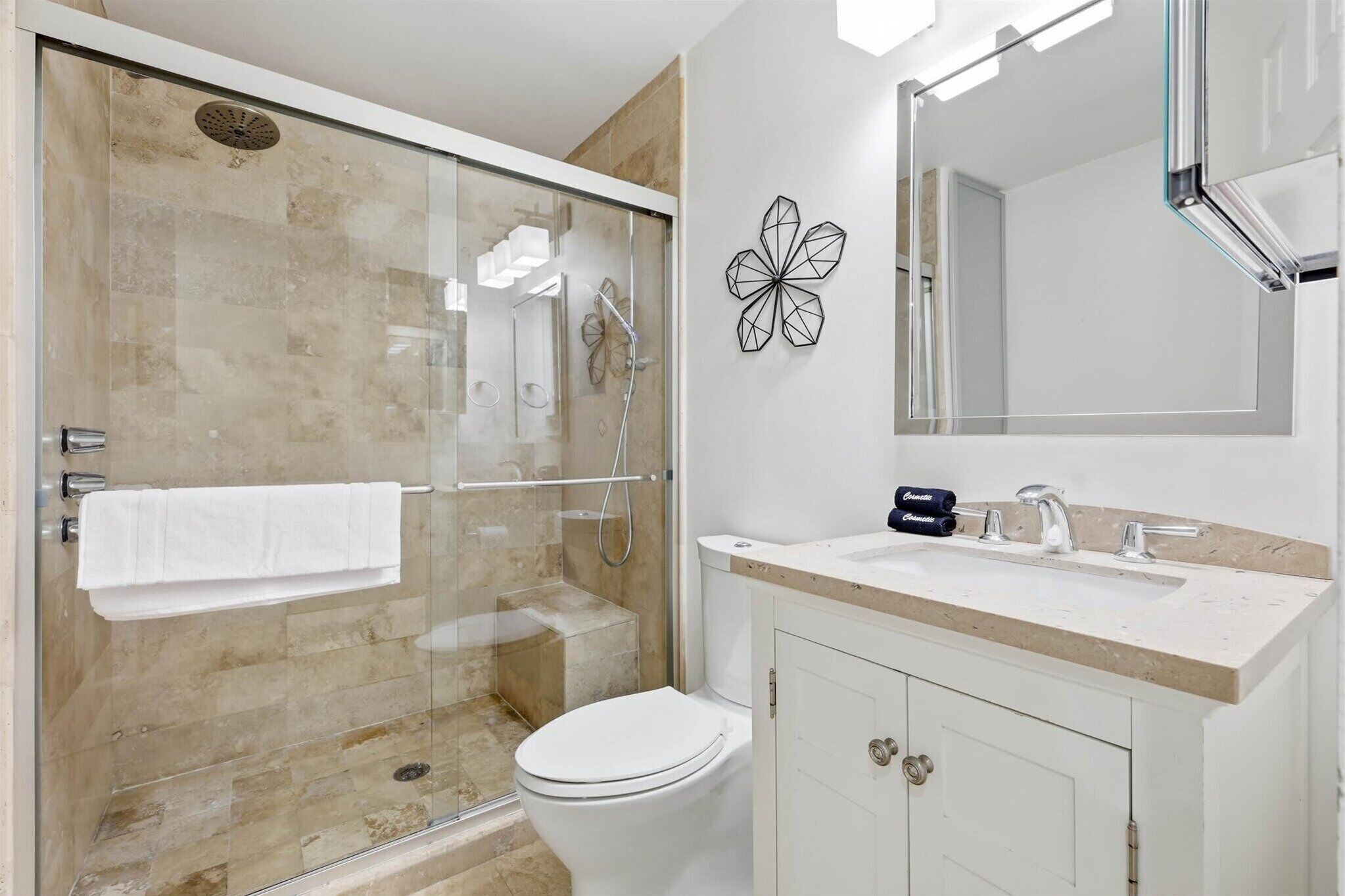 A bathroom with a glass-enclosed shower, a white toilet, a sink with a faucet, and a mirror above the sink.