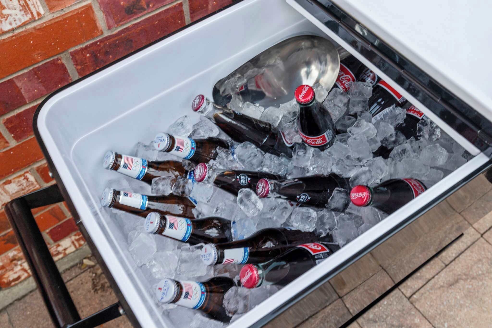 Un récipient en métal rempli de glace, de bouteilles de bière et de boissons gazeuses.