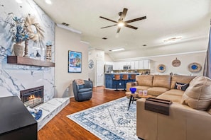 A living room with a fireplace, leather sofa, and a kitchen in the background. - Luxury 2 King beds, Hot Tub, near PGA & Universal (Frisco)