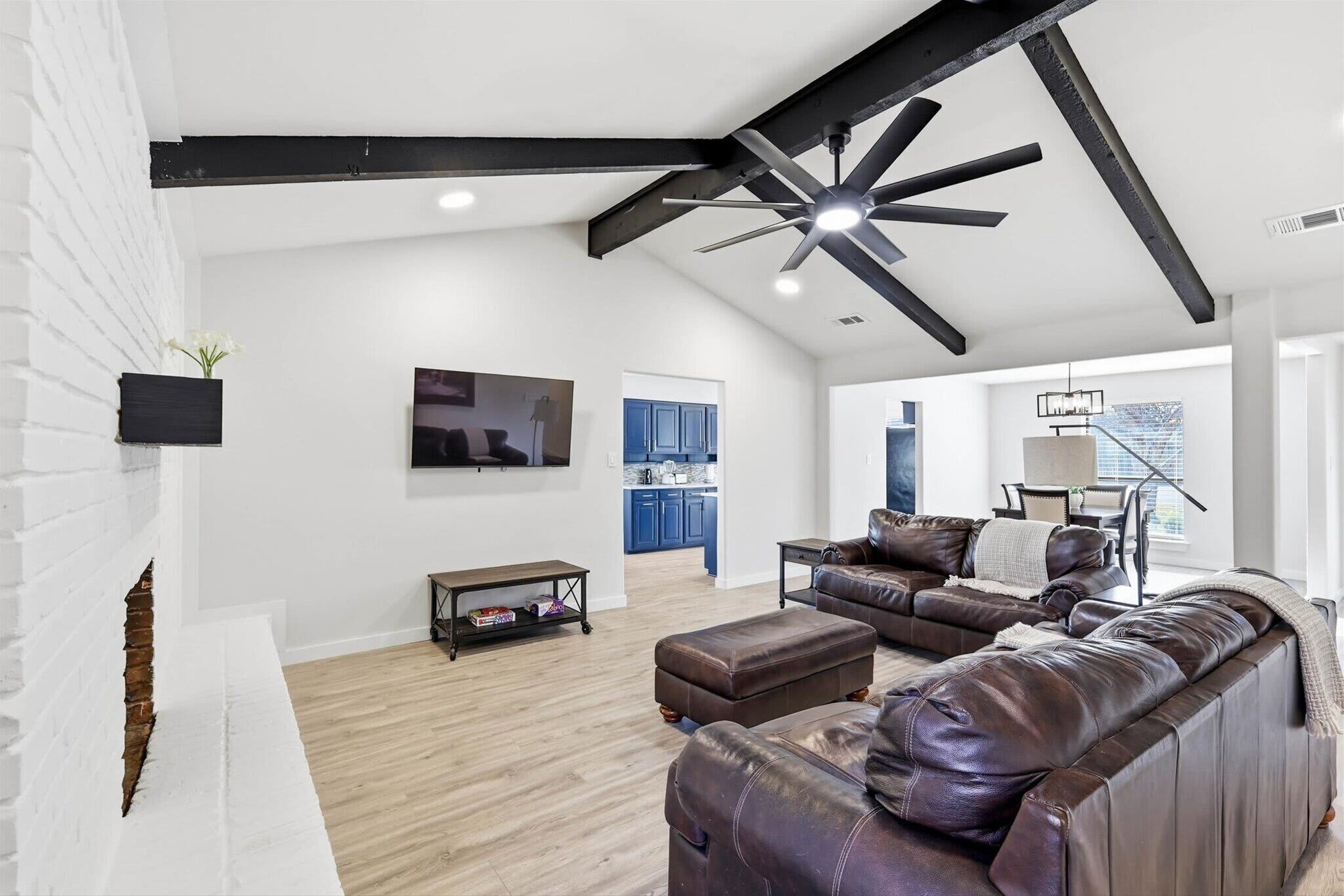 A spacious living area with a fireplace, leather sofa, and a ceiling fan.