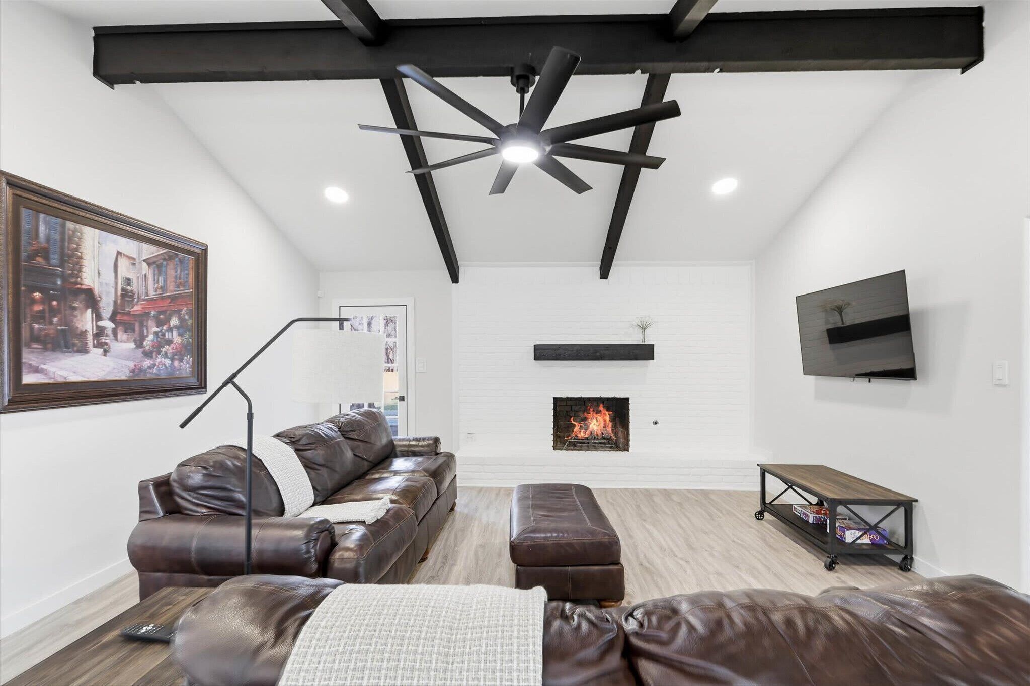 A modern living room with a fireplace, leather furniture, a ceiling fan, and a mounted TV.