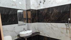 A bathroom with a white sink, black marble walls, a mirror, and a toilet. - Hotel funday (Jaipur)