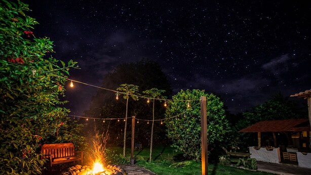 A nighttime outdoor setting with a stone fire pit, string lights, and a wooden bench.