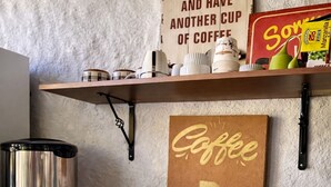 A coffee station with a coffee maker, cups, and a sign that says 'KEEP CALM AND HAVE ANOTHER CUP OF COFFEE.'
