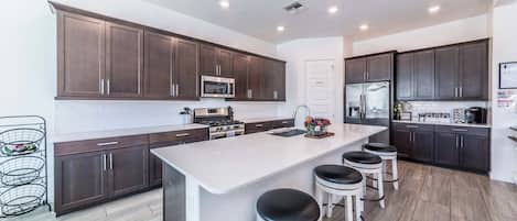A modern kitchen with dark wood cabinets, stainless steel appliances, a central island with stools, and a white backsplash.