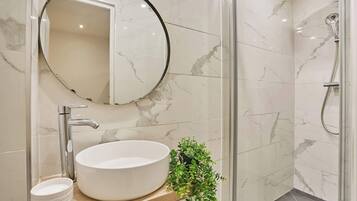 Un baño con un espejo redondo, un lavabo de pedestal, una ducha y una pequeña planta en maceta.