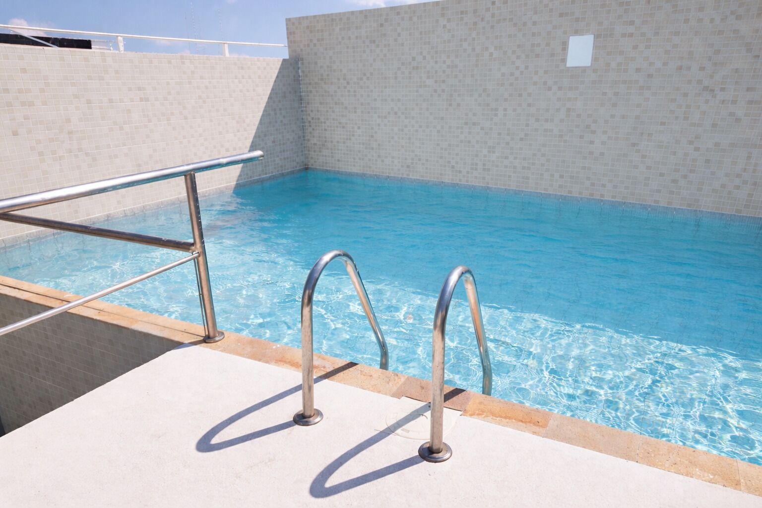 A swimming pool with metal railings and a tiled wall.