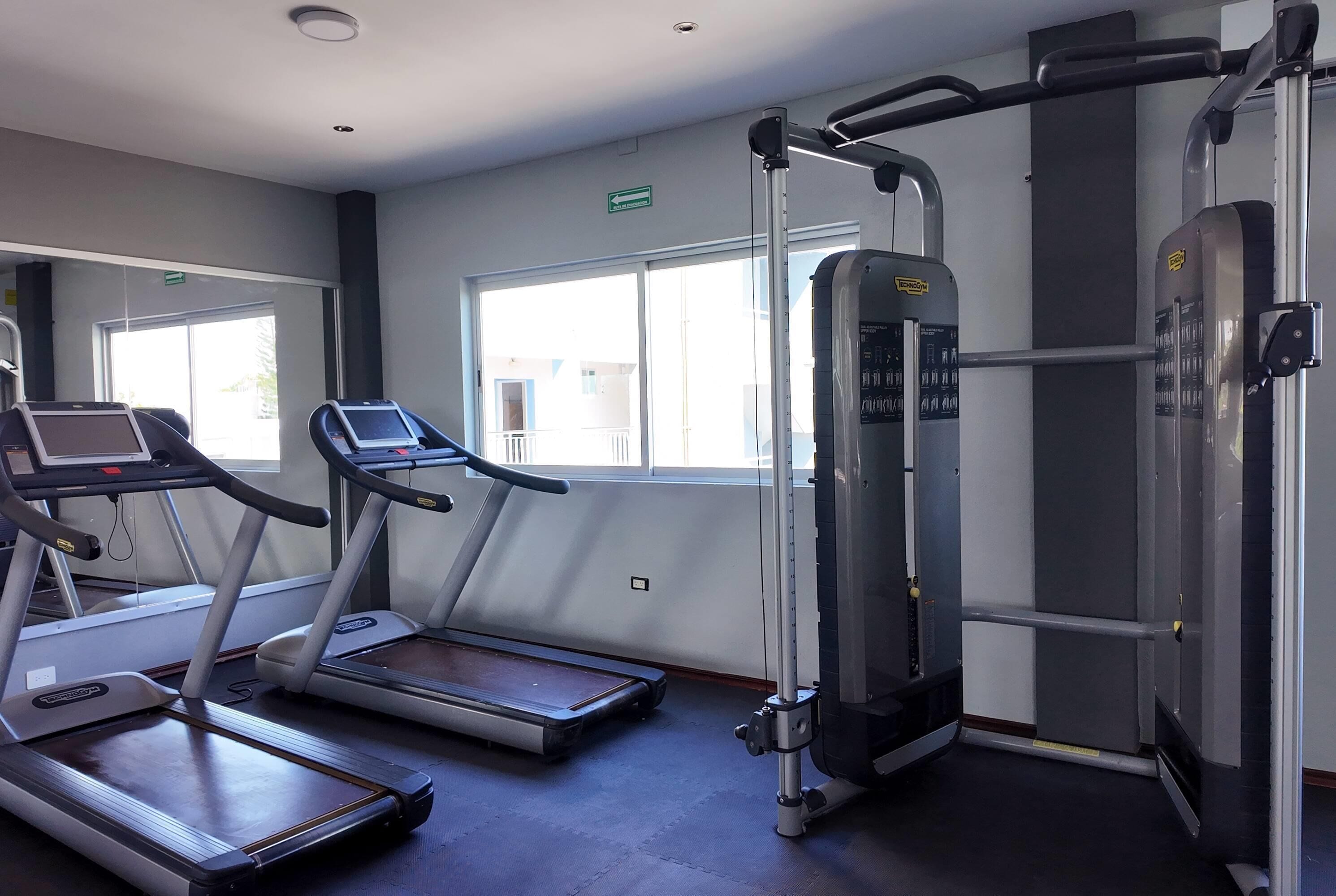 Un gimnasio con cintas de correr, máquinas de pesas y un ventanal amplio.
