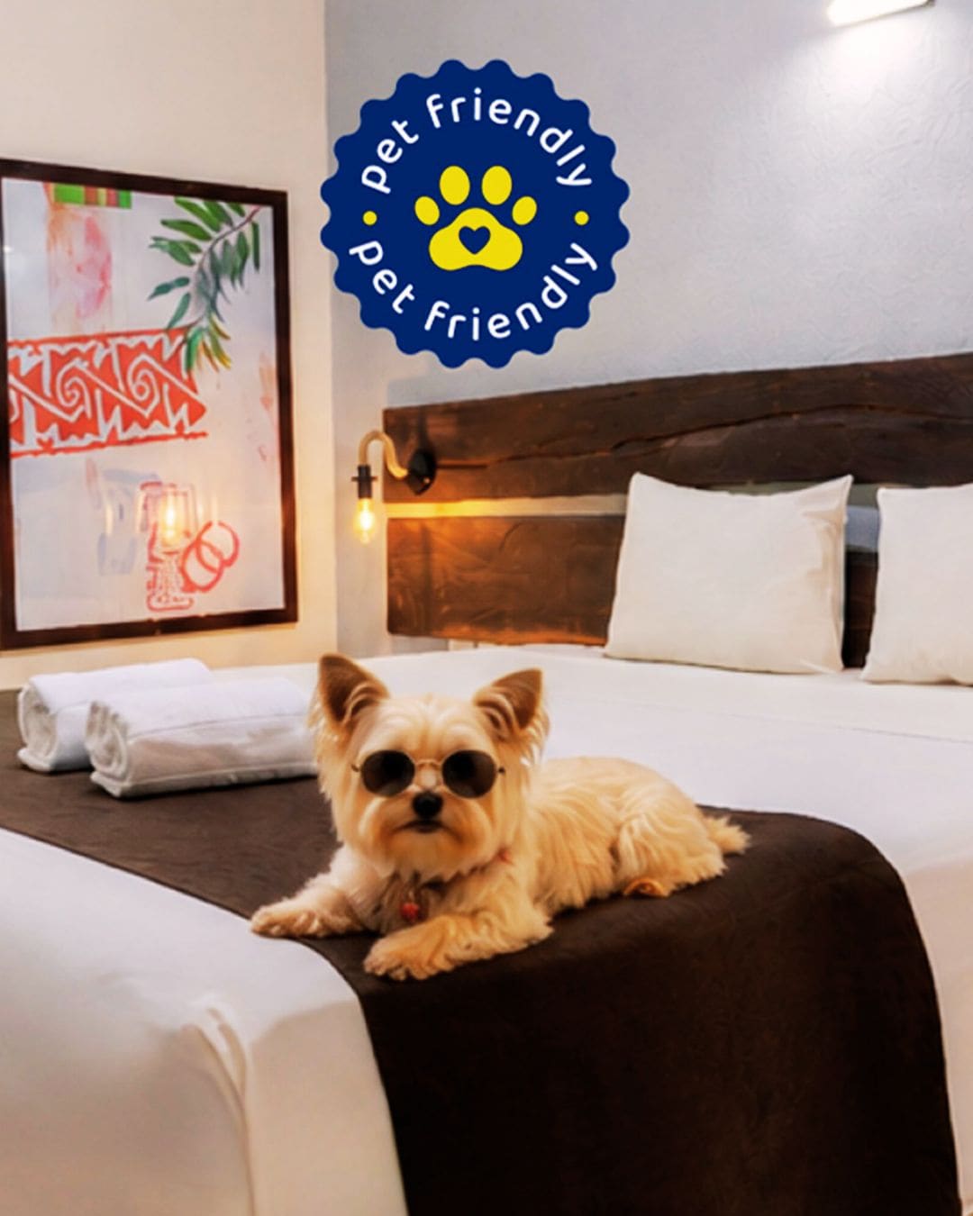 A pet-friendly hotel room with a bed, a framed picture, and a wall-mounted light.
