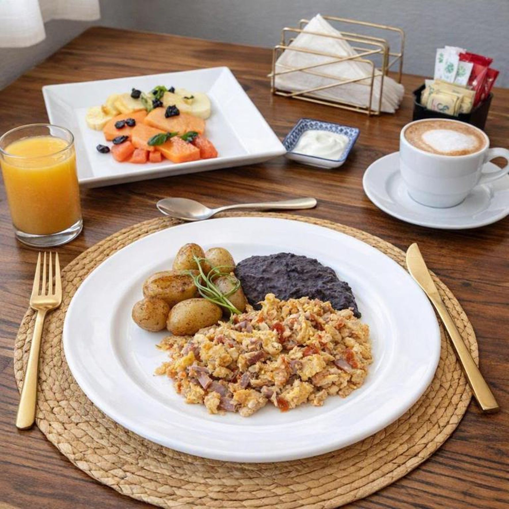 Un plato de desayuno con huevos, papas, frijoles negros y un vaso de jugo de naranja.