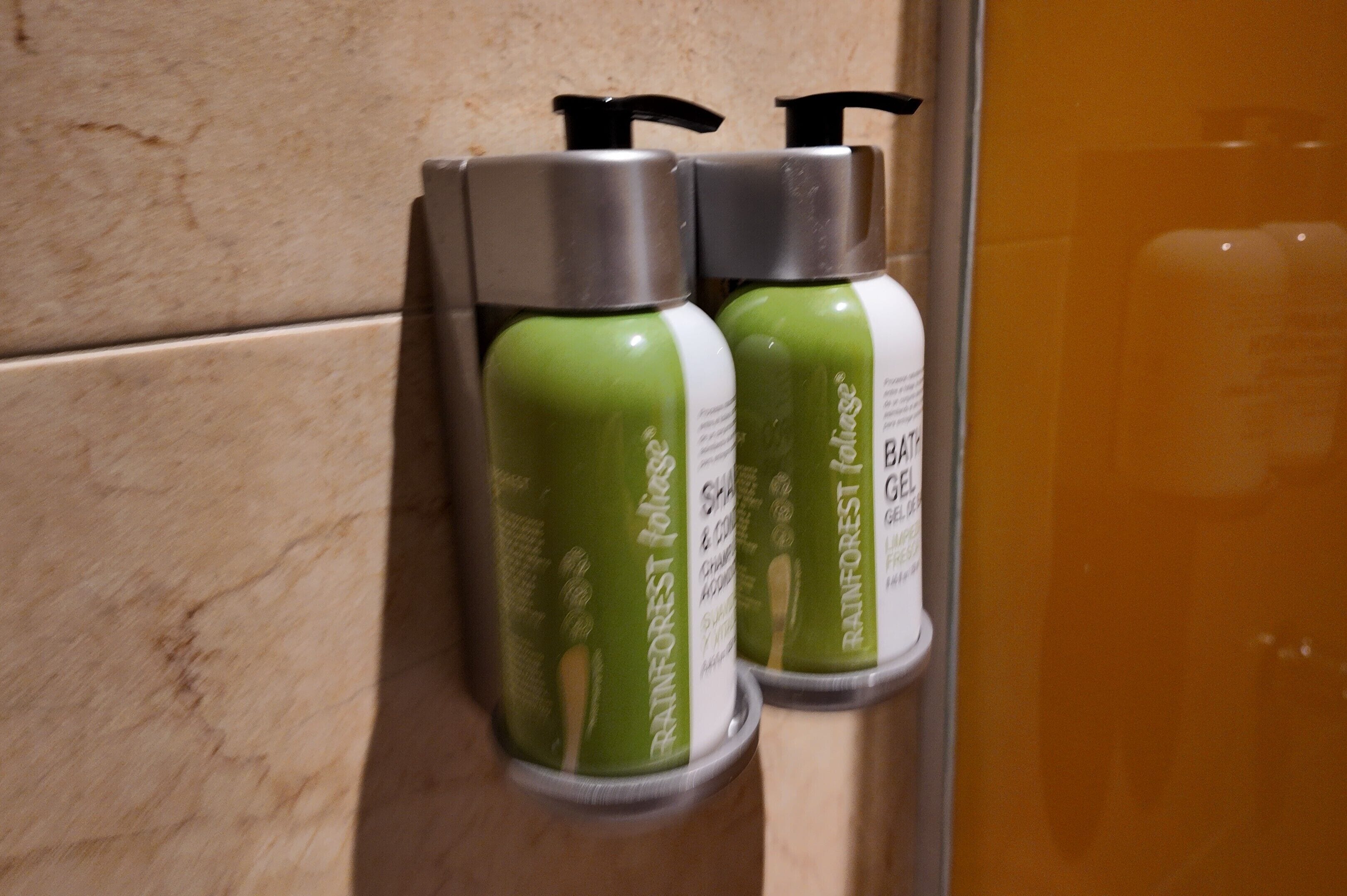 Zwei grüne Flaschen mit Pumpen, beschriftet mit 'Rainforest Gel', an einer gefliesten Wand.