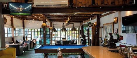 Una sala de billar con mesa de pool, luces colgantes y un televisor mostrando la Copa Mundial 2026.