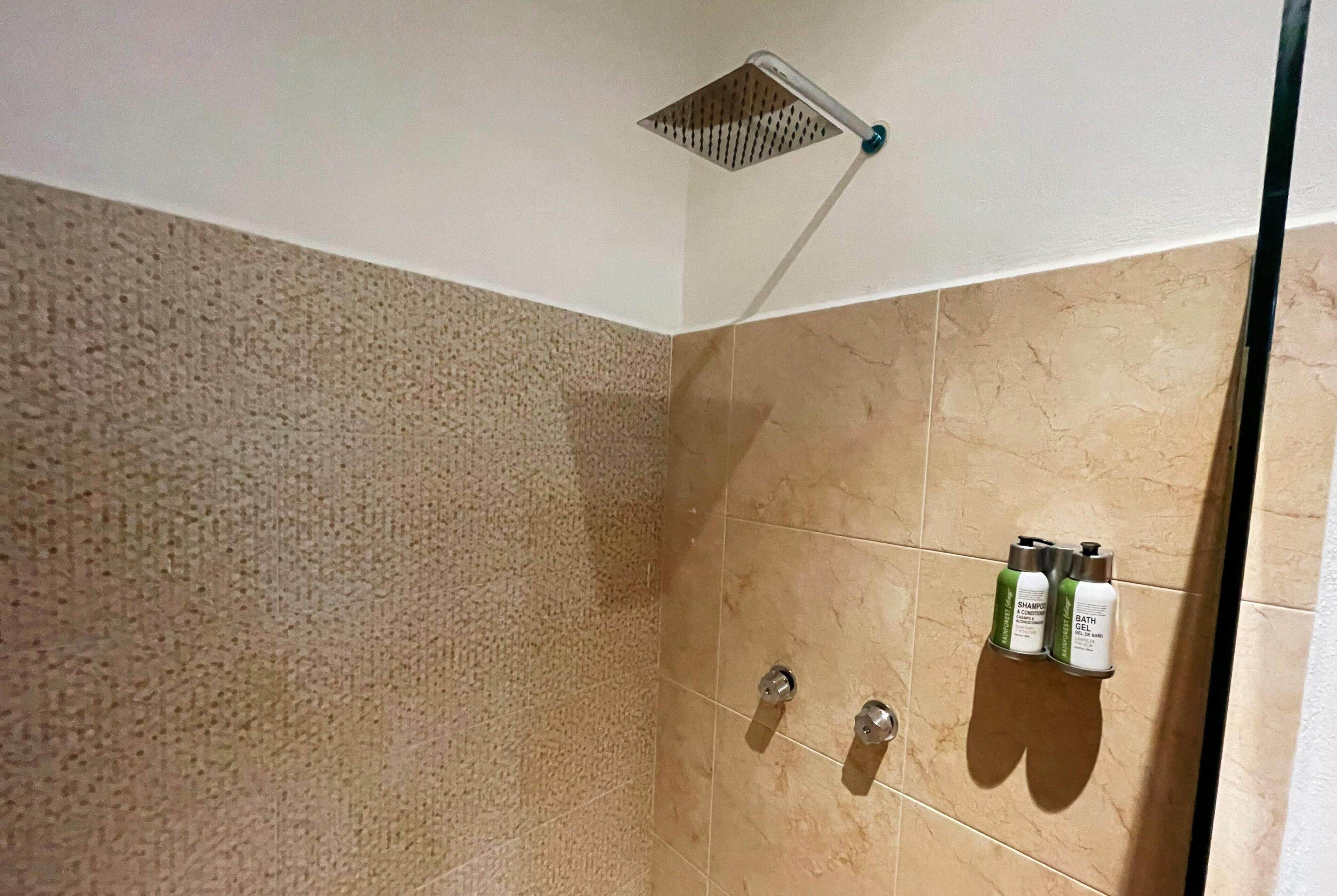 A shower with a square drain, beige textured walls, and two bottles of shampoo and bath products.