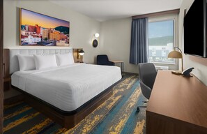 A hotel room with a large bed, a desk, a chair, a TV, and a painting of a cityscape. - La Quinta Inn & Suites By Wyndham Roanoke Hollins/I-81 (Roanoke)