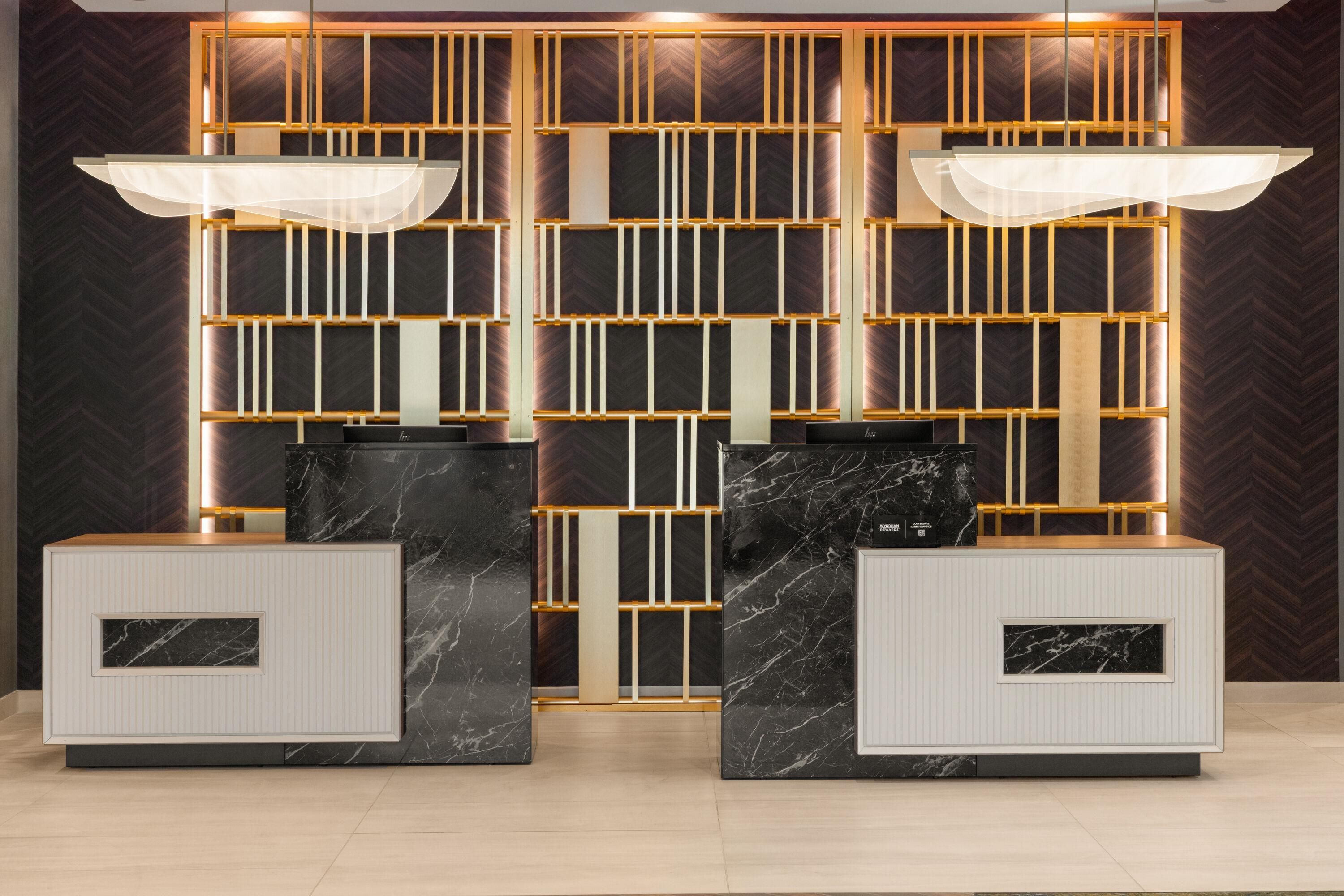 Un espace d’accueil au design moderne, avec un mur à motifs foncés, un luminaire aux formes géométriques et des comptoirs d’accueil surmontés de marbre.