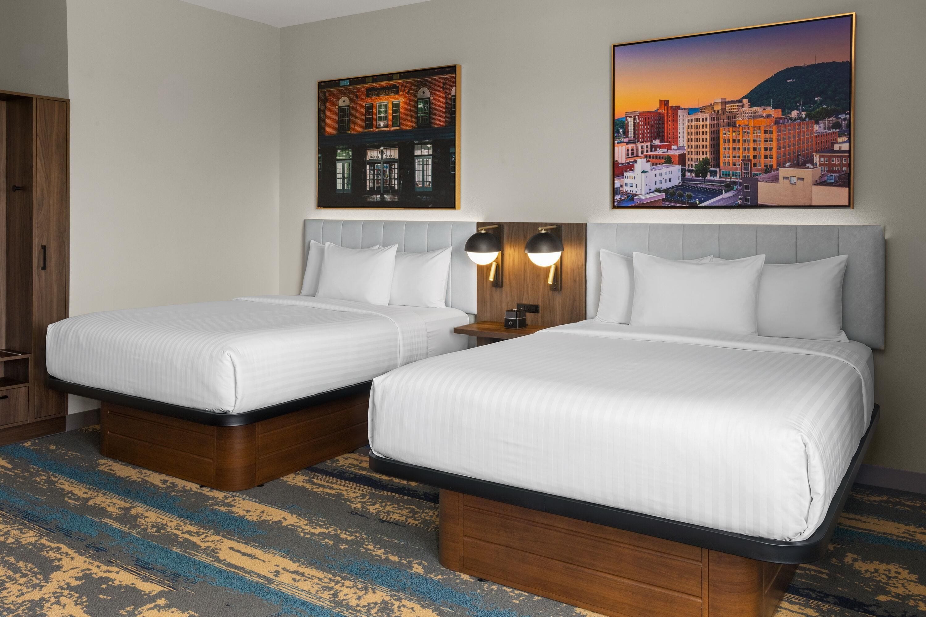 Een hotelkamer met twee bedden, een houten hoofdeinde, een stadsgezicht schilderij en een schilderij van een stadsmarkt.