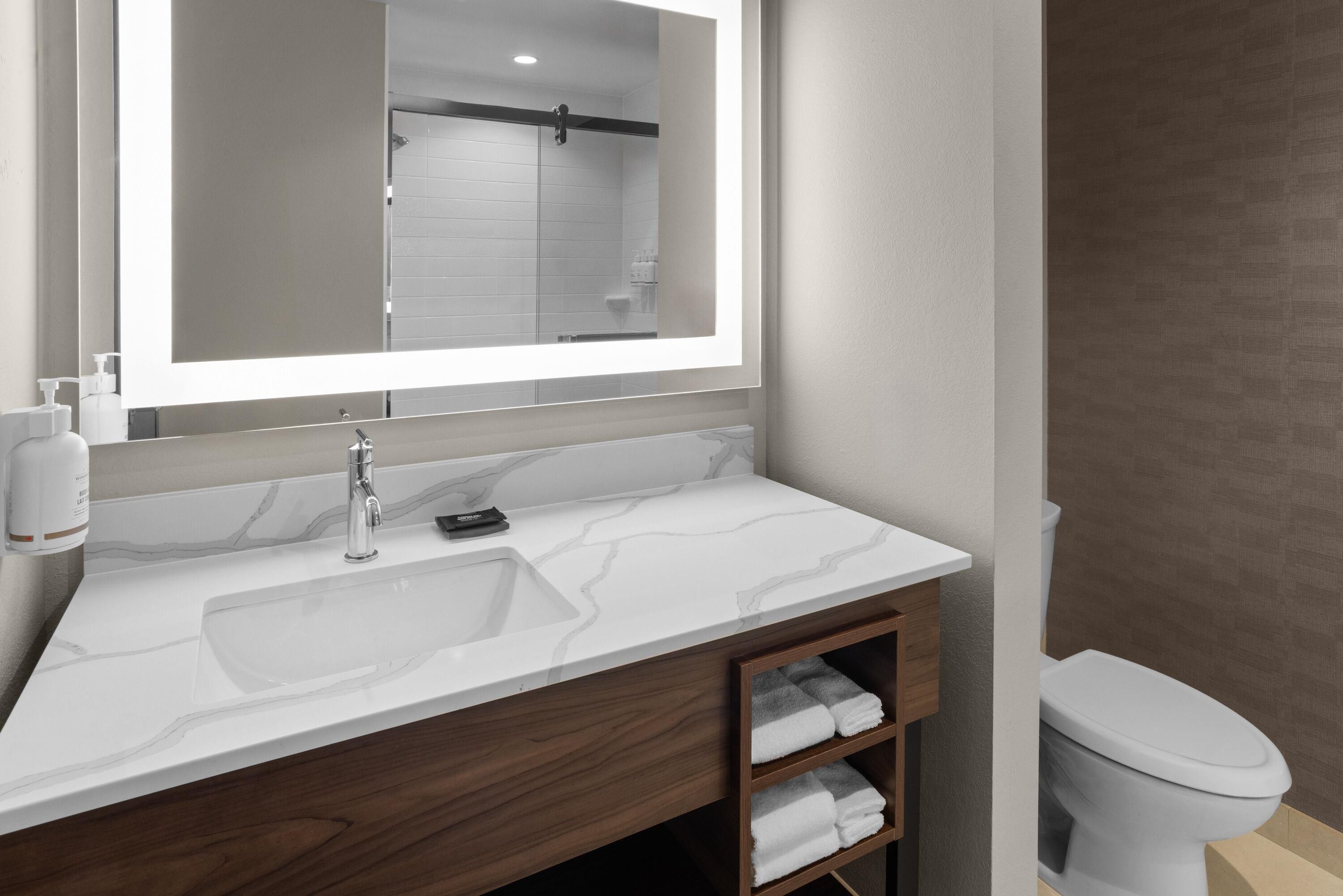 A bathroom with a marble sink, a mirror, a toilet, and a shelf with towels.