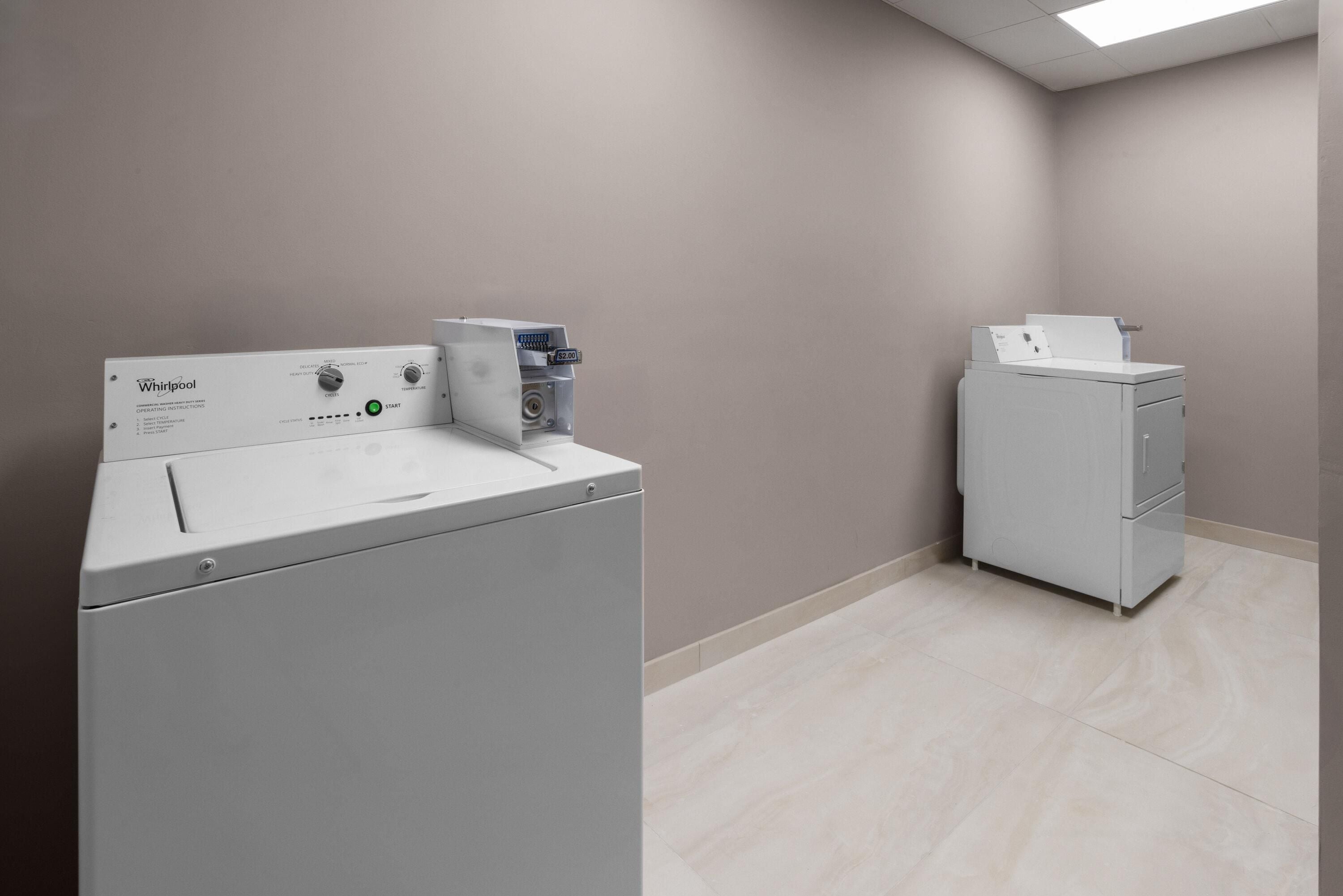 Un cuarto de lavandería con lavadora y secadora Whirlpool de carga frontal, un armario de servicios y piso de baldosas.