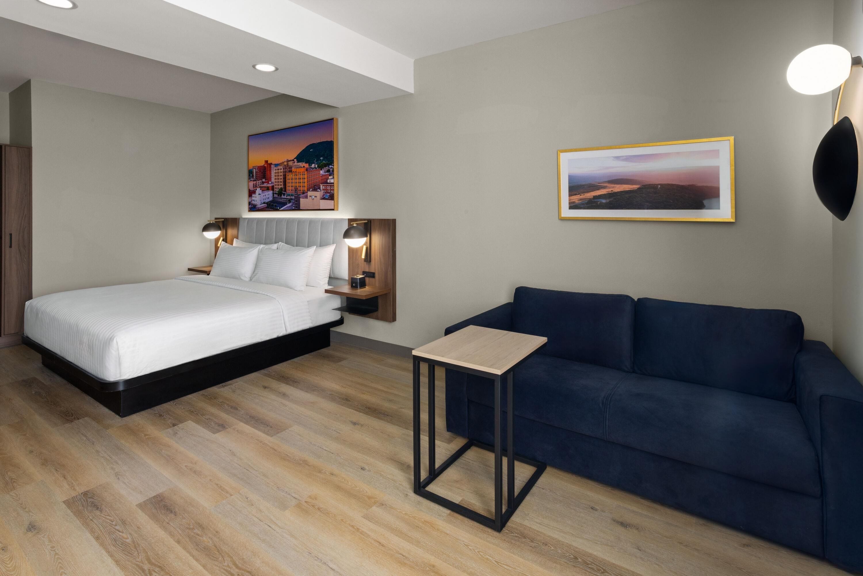 A modern hotel room with a bed, a small table, a sofa, and two wall-mounted lamps.