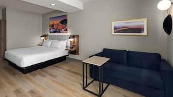 A modern hotel room with a bed, a small table, a sofa, and two wall-mounted lamps.