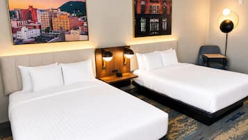 A hotel room with two beds, a nightstand, a lamp, and two wall-mounted pictures.