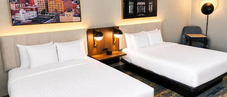 Une chambre d’hôtel avec deux lits, une table de chevet, une lampe et deux tableaux accrochés au mur.