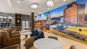 A modern lounge area with seating, a coffee bar, and a cityscape mural on the wall.