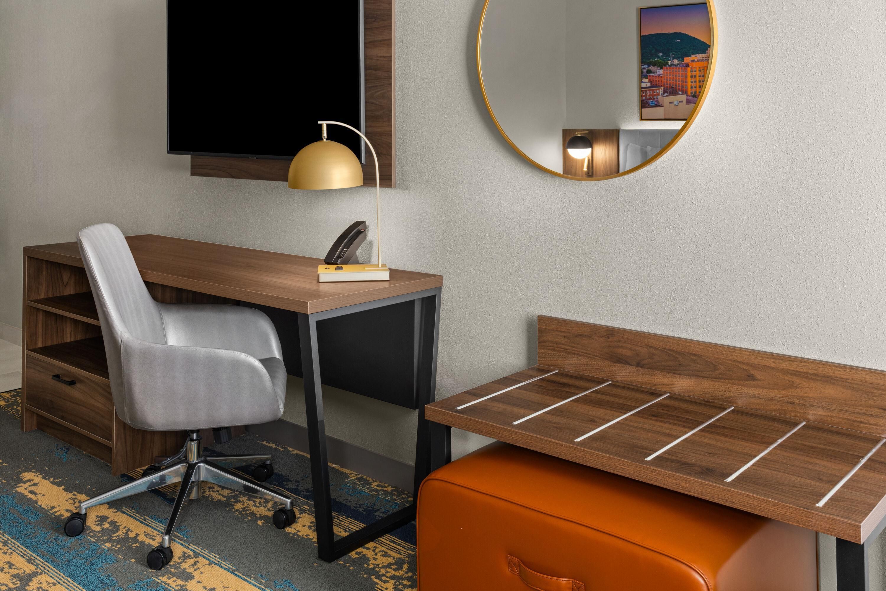 A modern room with a desk, chair, and a small orange ottoman.