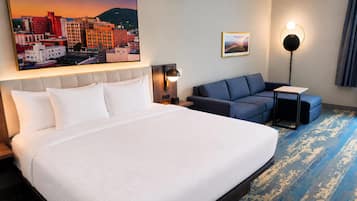 Een hotelkamer met een groot bed, een bank, een kleine tafel, een lamp en een stadslandschap schilderij aan de muur.