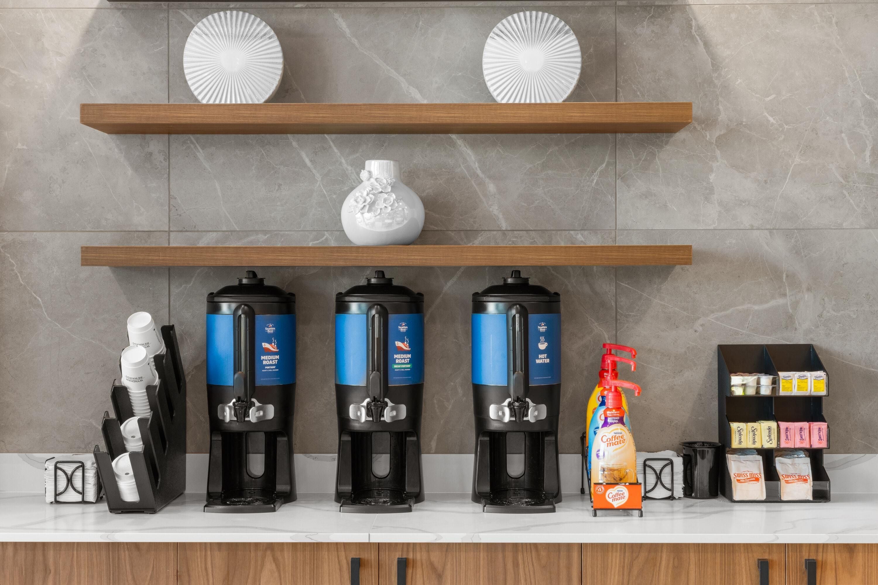 Uma estação de café com três dispensadores, um dispensador com bomba vermelha e uma caixa de cápsulas de café.
