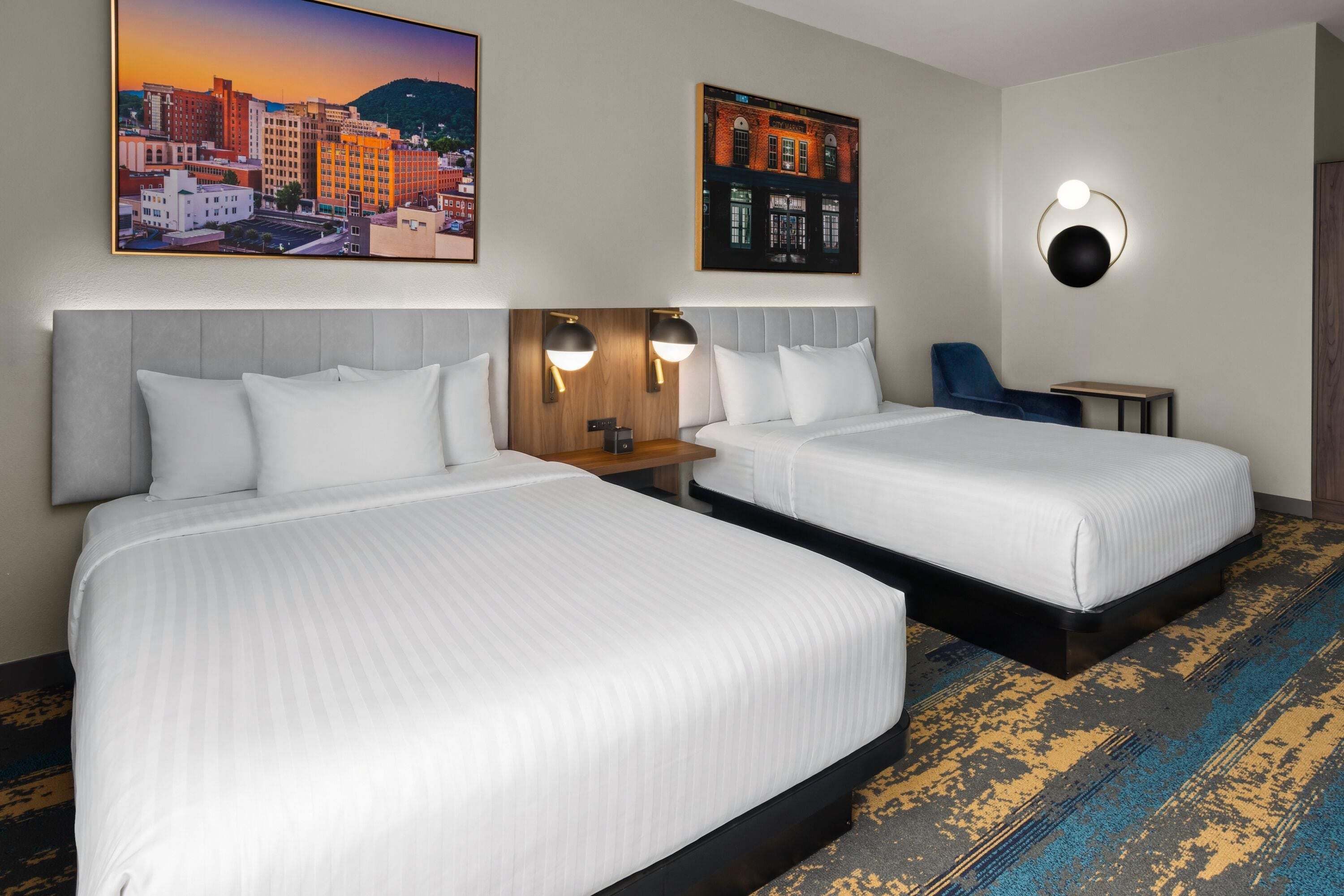A hotel room with two beds, a nightstand, a chair, and two wall-mounted lamps.