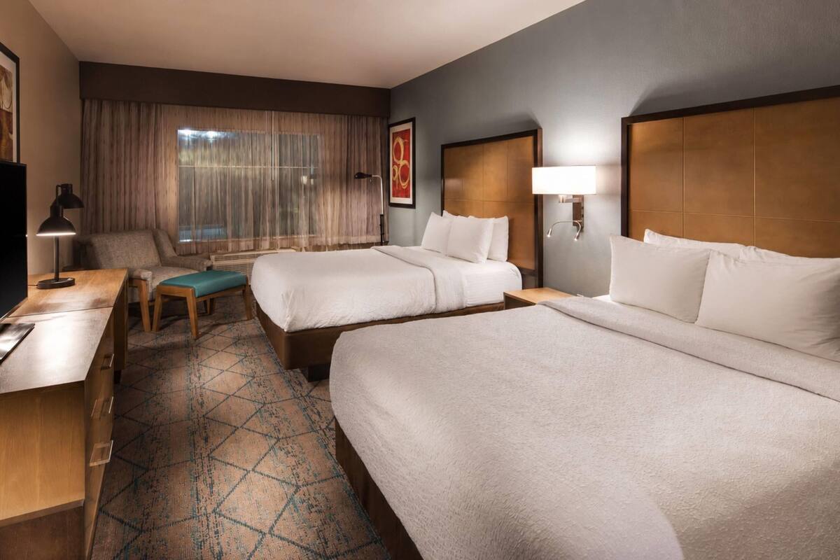 A hotel room with two beds, a desk, a chair, a TV, and a window with curtains.