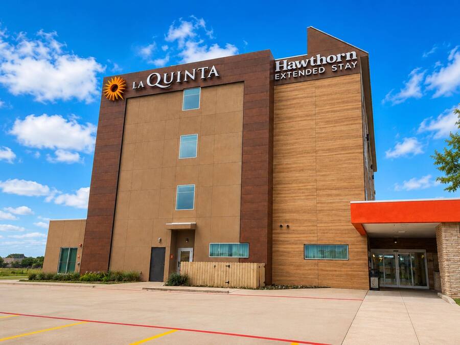 Um hotel com design moderno, apresentando um logotipo de sol em destaque e o nome 'La Quinta Hawthorn Extended Stay'.