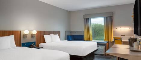Habitación de hotel con dos camas, un escritorio, un televisor y una ventana con cortinas.