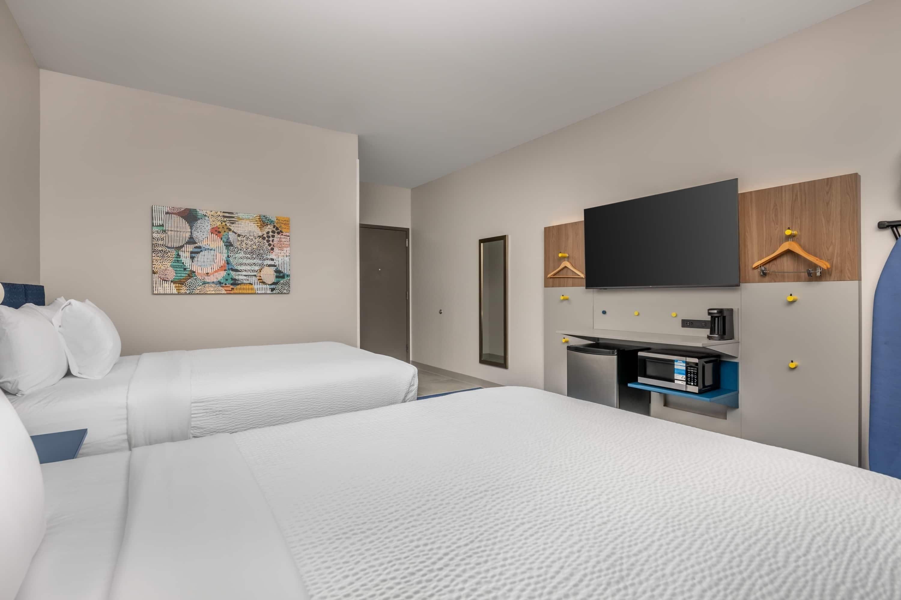 A hotel room with two beds, a television, a small kitchenette, and a door.