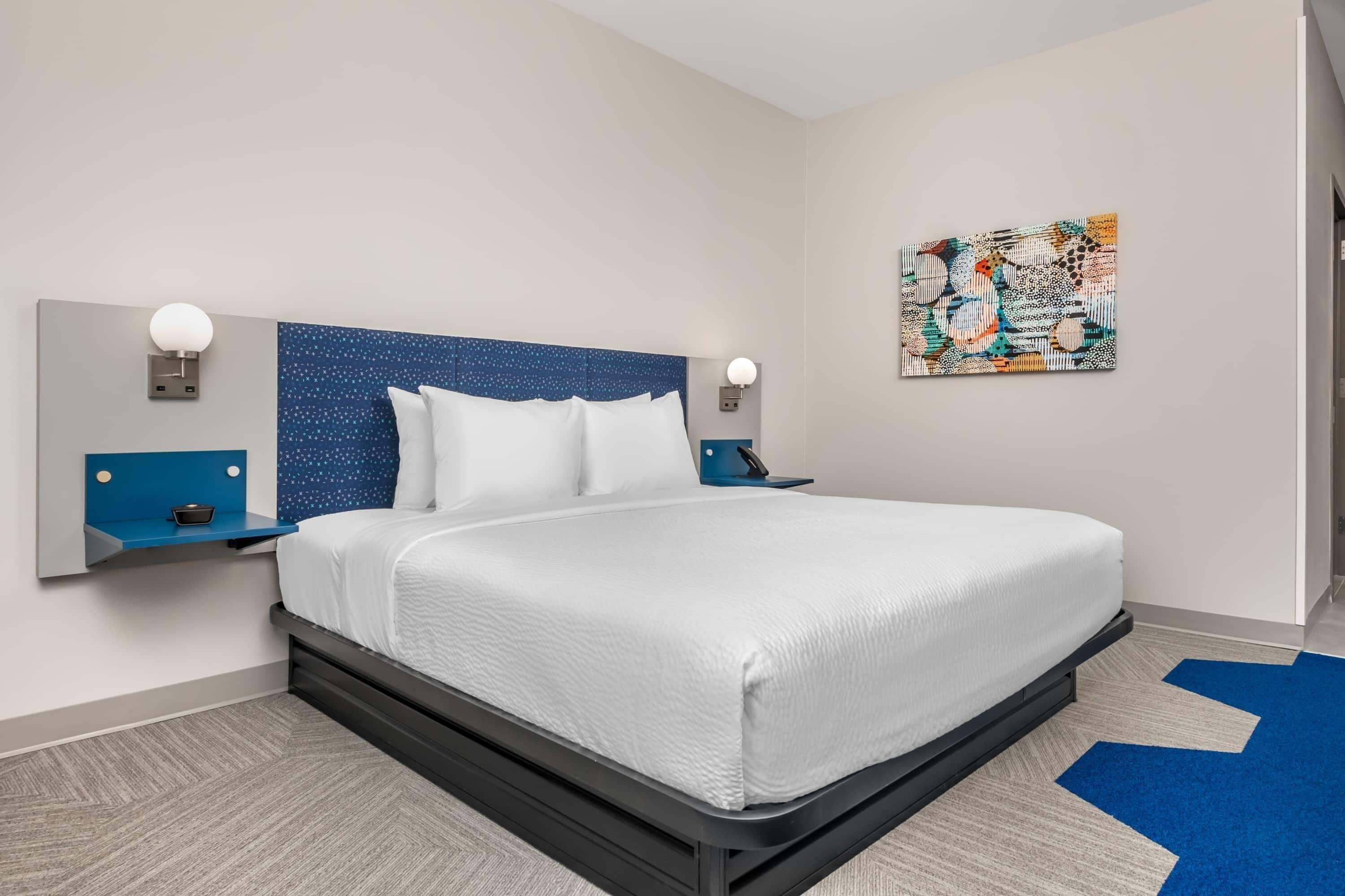 A modern hotel room with a large bed, two bedside tables, a headboard with a star pattern, and a wall-mounted artwork.