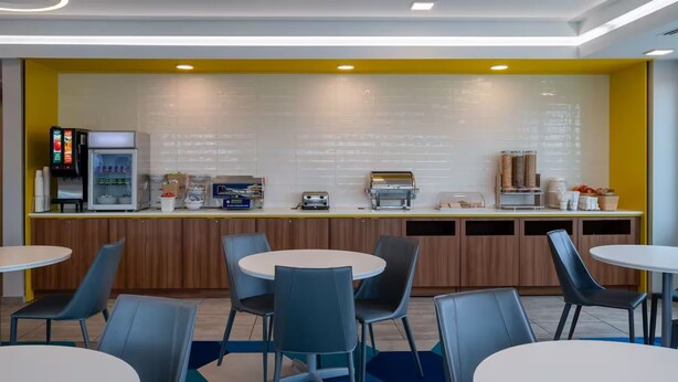 Un café moderne avec un mur d’accent jaune, une machine à café, un réfrigérateur et un espace salon.