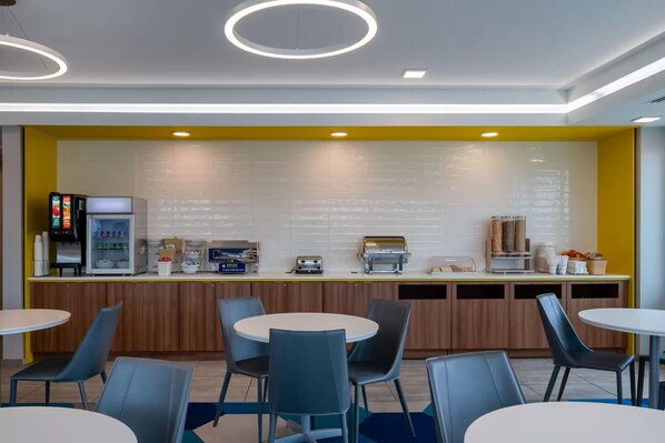 Un café moderno con una pared de acento amarillo, una máquina de café, un refrigerador y una zona de estar.