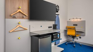 Une chambre d’hôtel équipée d’un téléviseur à écran plat, d’une machine à café, d’un four à micro-ondes, d’un bureau, d’une chaise et d’une moquette bleue.