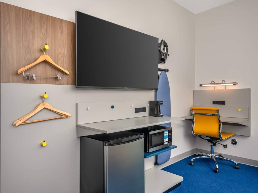 Habitació d'hotel amb televisió de pantalla plana, màquina de cafè, microones, escriptori, cadira i una catifa blava.