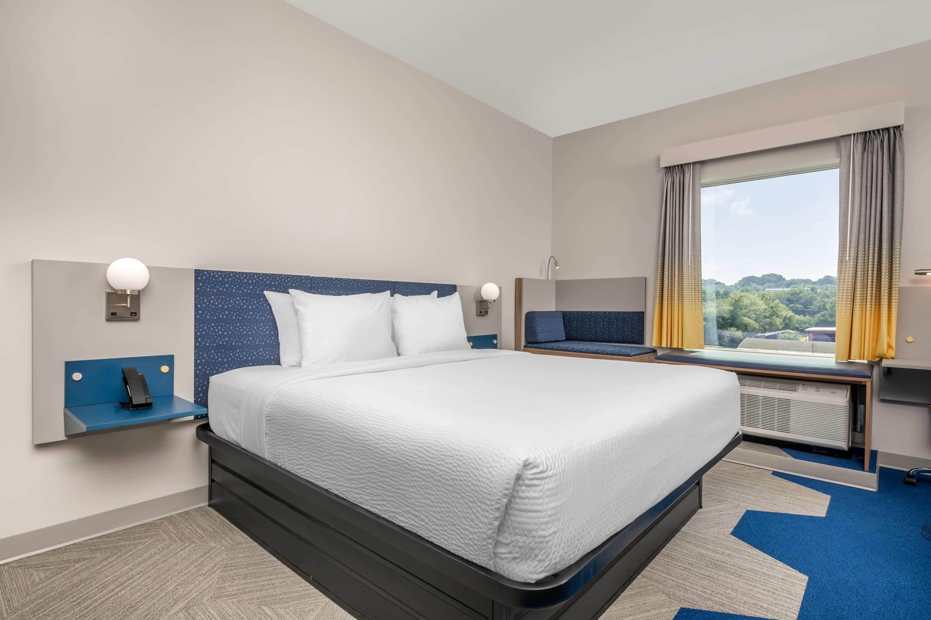 Une chambre d’hôtel avec un grand lit, un bureau, une chaise, une fenêtre avec des rideaux et une vue sur l’extérieur.